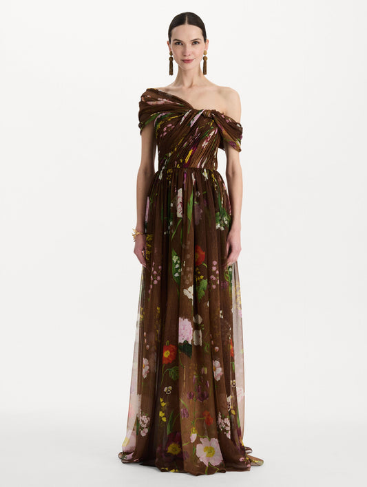 The model is wearing the mixed botanical silk chiffon gown with a one-shoulder neckline and a painterly floral print in a brown multi palette. Front view.