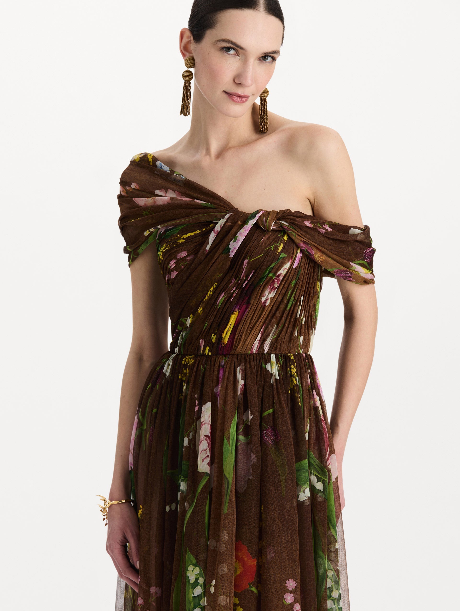 The model is wearing the mixed botanical silk chiffon gown with a one-shoulder neckline and a painterly floral print in a brown multi palette. Zoom view.