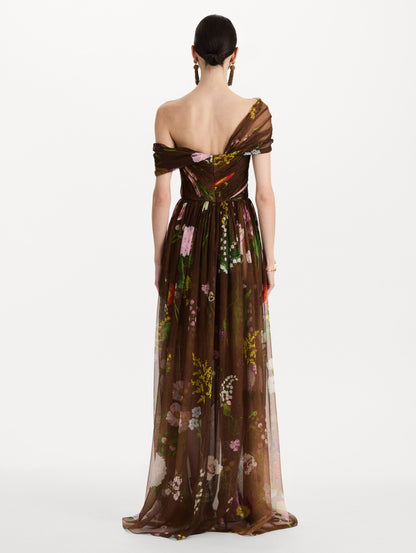The model is wearing the mixed botanical silk chiffon gown with a one-shoulder neckline and a painterly floral print in a brown multi palette. Back view.