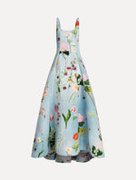 The model is wearing the mixed botanical faille gown with a sleeveless scoop neckline and a bold floral print in blue multi.