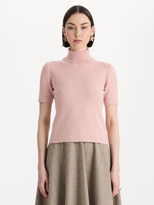 The model is wearing the turtleneck wool short-sleeve pullover with a fold-over neckline in the color blush. Front view.