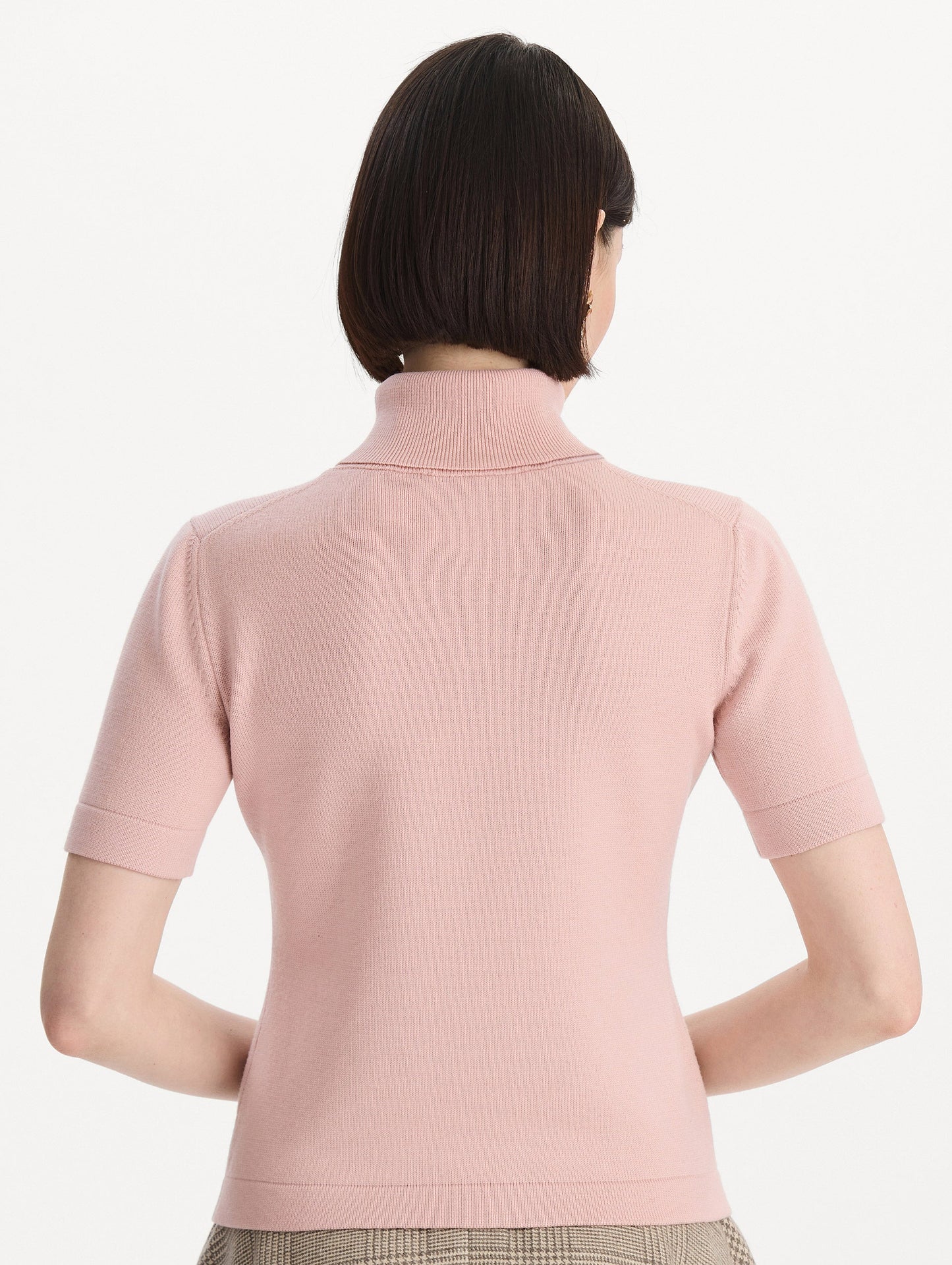 The model is wearing the turtleneck wool short-sleeve pullover with a fold-over neckline in the color blush. Back view.