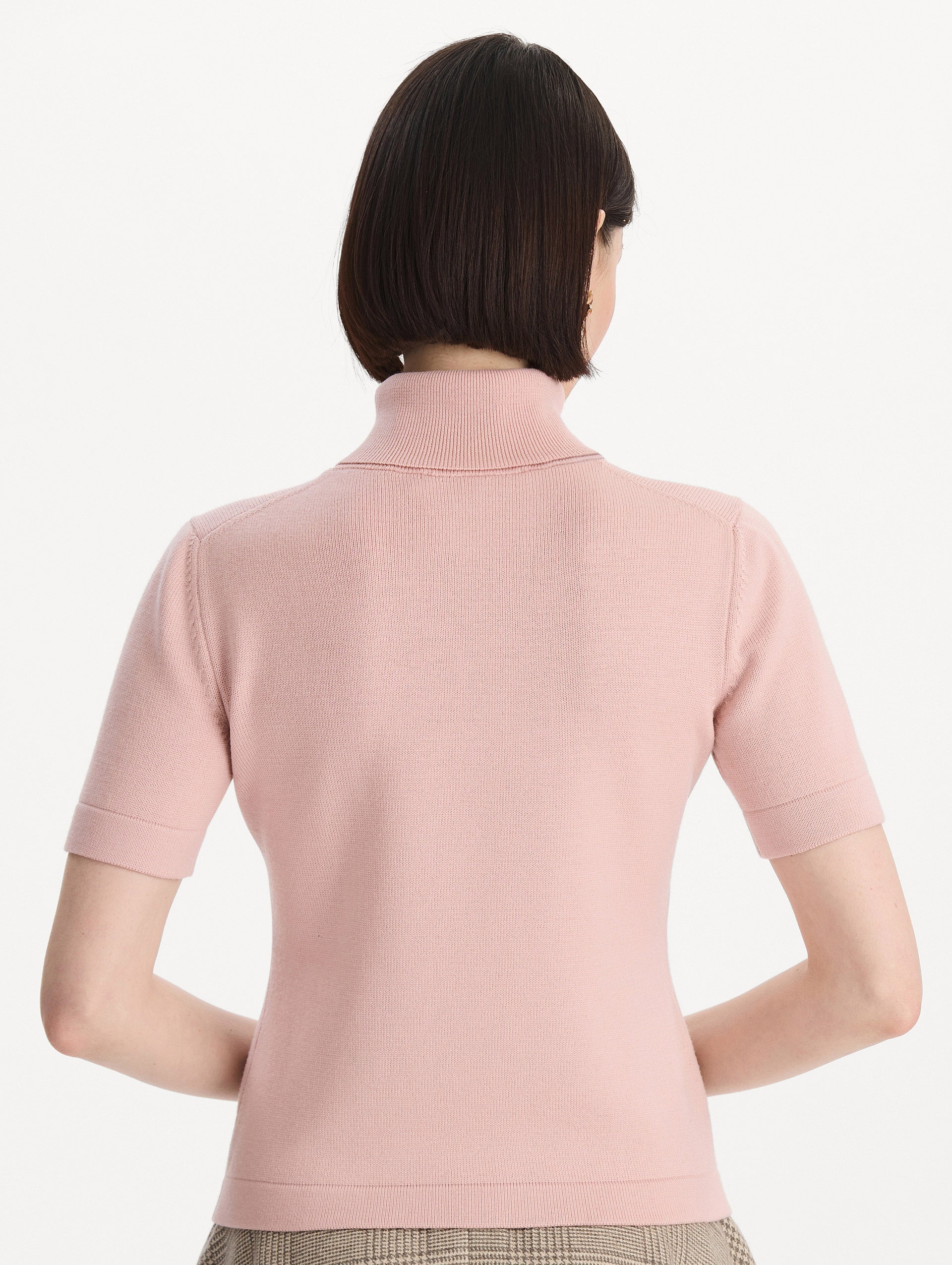 The model is wearing the turtleneck wool short-sleeve pullover with a fold-over neckline in the color blush. Back view.