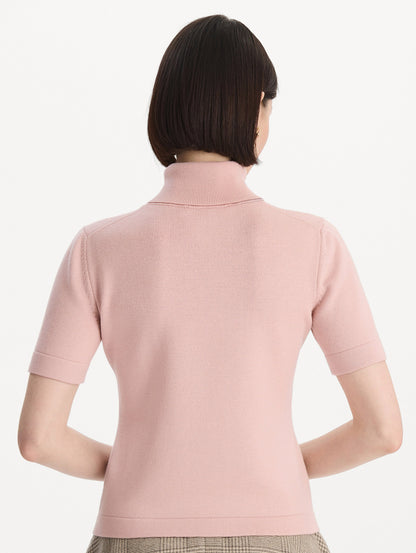 The model is wearing the turtleneck wool short-sleeve pullover with a fold-over neckline in the color blush. Back view.