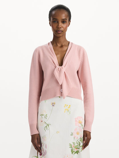 The model is wearing the tie-neck cardigan in blush wool with a tie V-neck detail. Front view.
