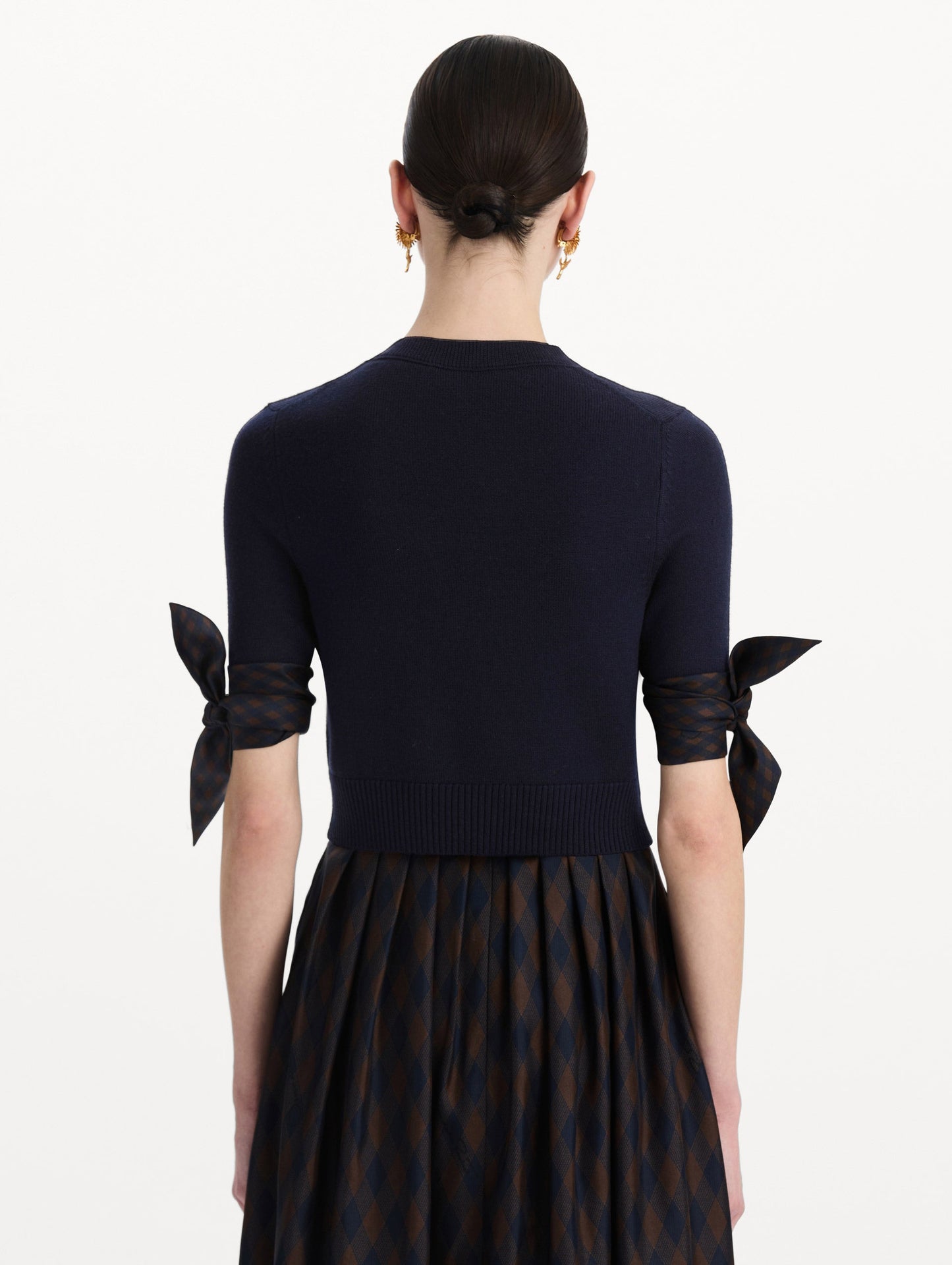 The model is wearing the argyle tie-detailed cardigan in the color navy. Back view.
