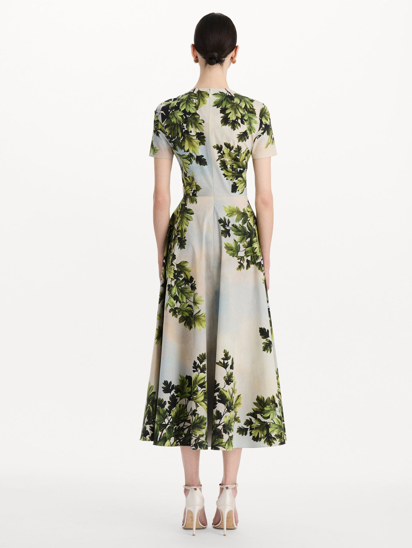 The model is wearing the maple leaves cotton poplin dress with short sleeves and an all-over foliage print in the color green multi. Back view.