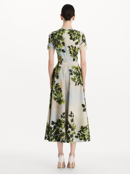 The model is wearing the maple leaves cotton poplin dress with short sleeves and an all-over foliage print in the color green multi. Back view.