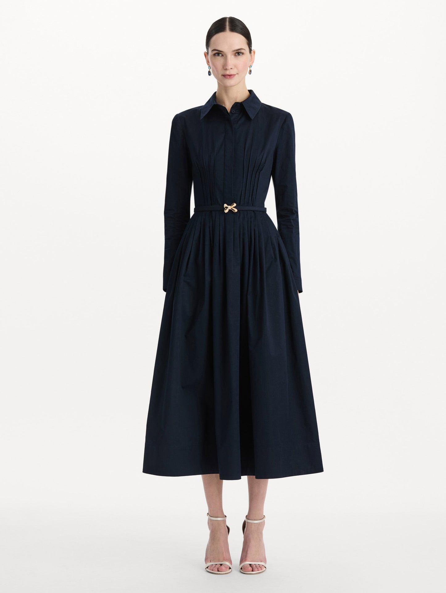 The model is wearing the bow belt cotton stretch twill dress with a collared neckline and long sleeves in the color navy. Front view.