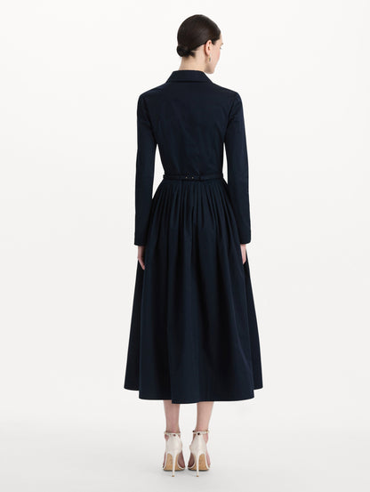 The model is wearing the bow belt cotton stretch twill dress with a collared neckline and long sleeves in the color navy. Back view.
