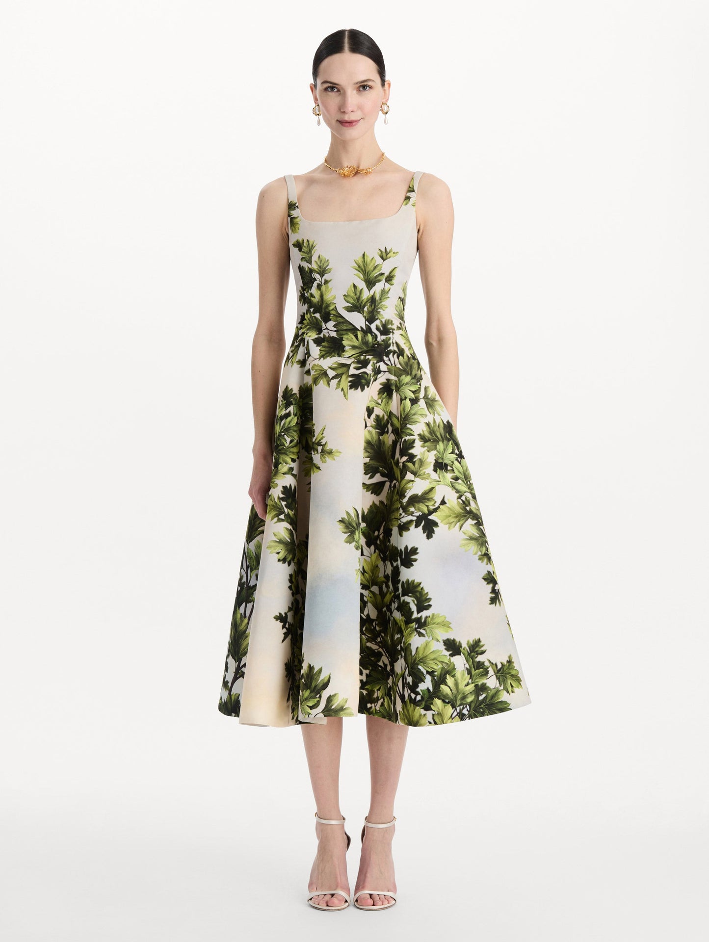 The model is wearing the maple leaves faille dress with a sleeveless scoop neckline and a foliage print in the color green multi. Front view.