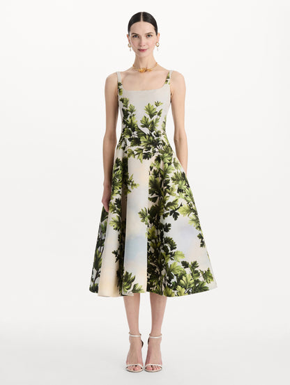 The model is wearing the maple leaves faille dress with a sleeveless scoop neckline and a foliage print in the color green multi. Front view.