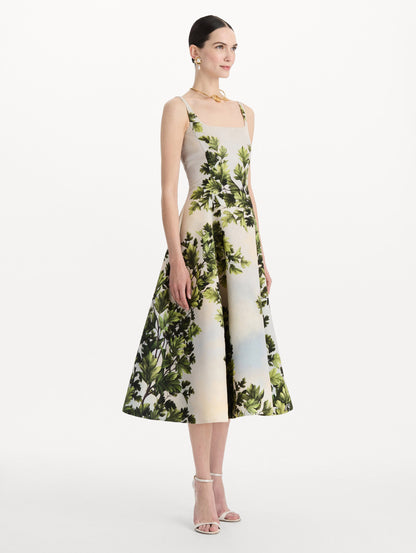 The model is wearing the maple leaves faille dress with a sleeveless scoop neckline and a foliage print in the color green multi. Side view.