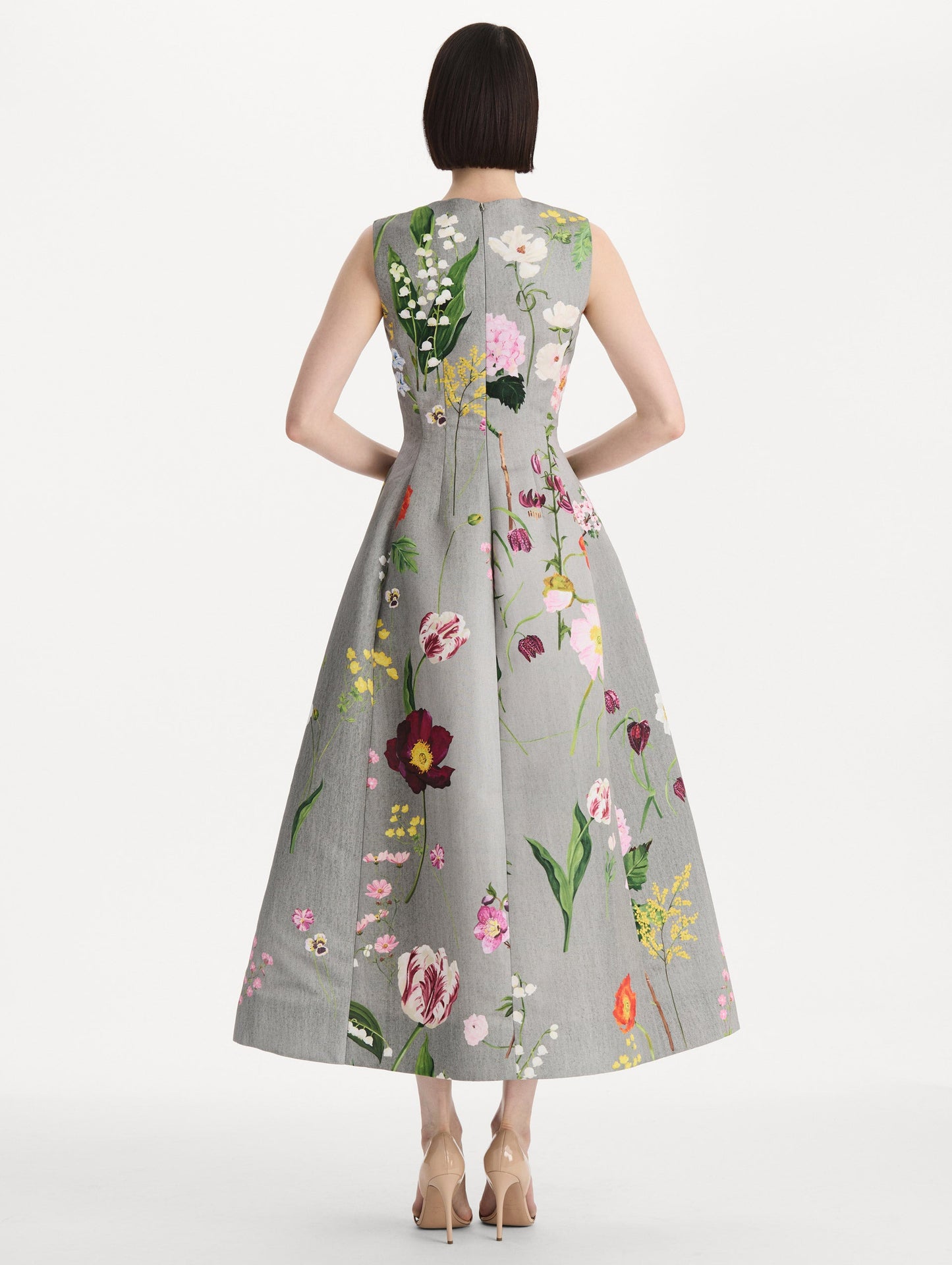 The model is wearing the mixed botanical faille cocktail dress with a sleeveless silhouette in the color grey multi. Back view.