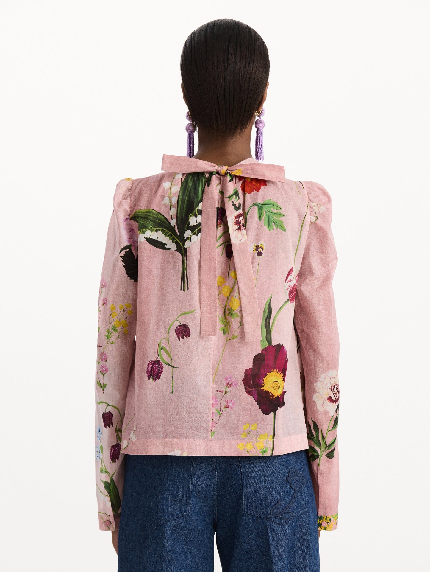 The model is wearing the mixed botanical tie-detailed blouse with a tie neckline and an all-over floral print in a blush multi palette. Back view.