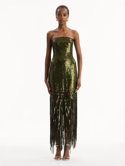 The model is wearing the Sequin Fringe Gown in green. Featuring a strapless neckline, fitted silhouette, and an open lattice detail cascading into a fringe skirt. Front View.