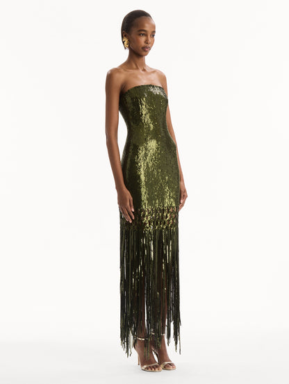 The model is wearing the Sequin Fringe Gown in green. Featuring a strapless neckline, fitted silhouette, and an open lattice detail cascading into a fringe skirt. Side View.