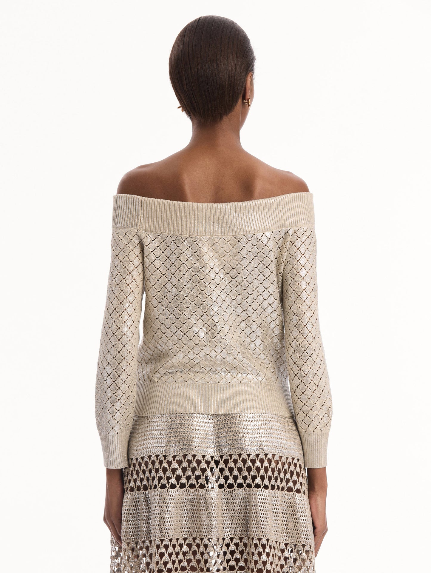 The model is wearing the Silver Foil Off-Shoulder Pullover. Featuring a lattice knit pattern, off-the-shoulder neckline, long sleeves, and ribbed trims. Back View.