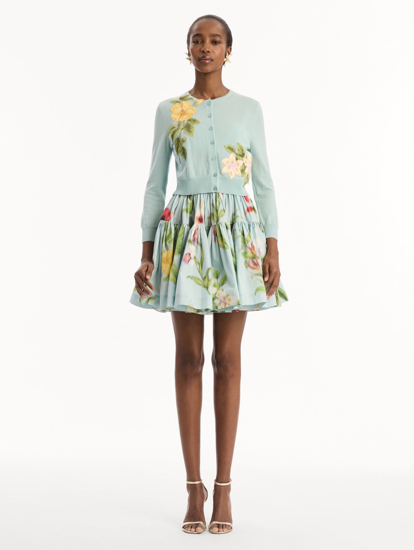 The model is wearing the Chiné Dominican Mixed-Floral Threadwork Cardigan in Saltwater Blue with threaded Dominican florals. Featuring buttons closures down the center, long sleeves, crew neckline, and ribbed trims. Front View.