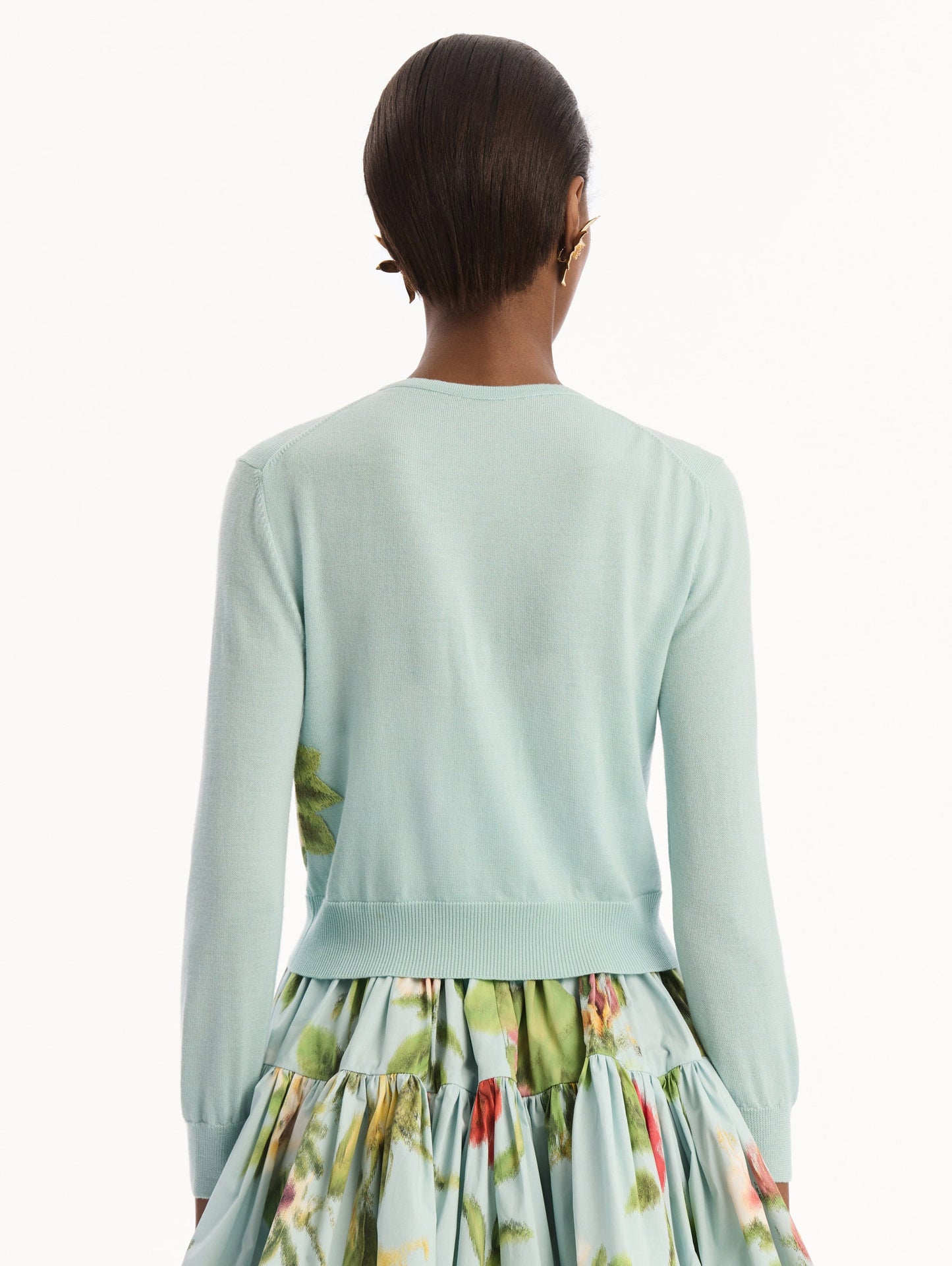 The model is wearing the Chiné Dominican Mixed-Floral Threadwork Cardigan in Saltwater Blue with threaded Dominican florals. Featuring buttons closures down the center, long sleeves, crew neckline, and ribbed trims. Back View.