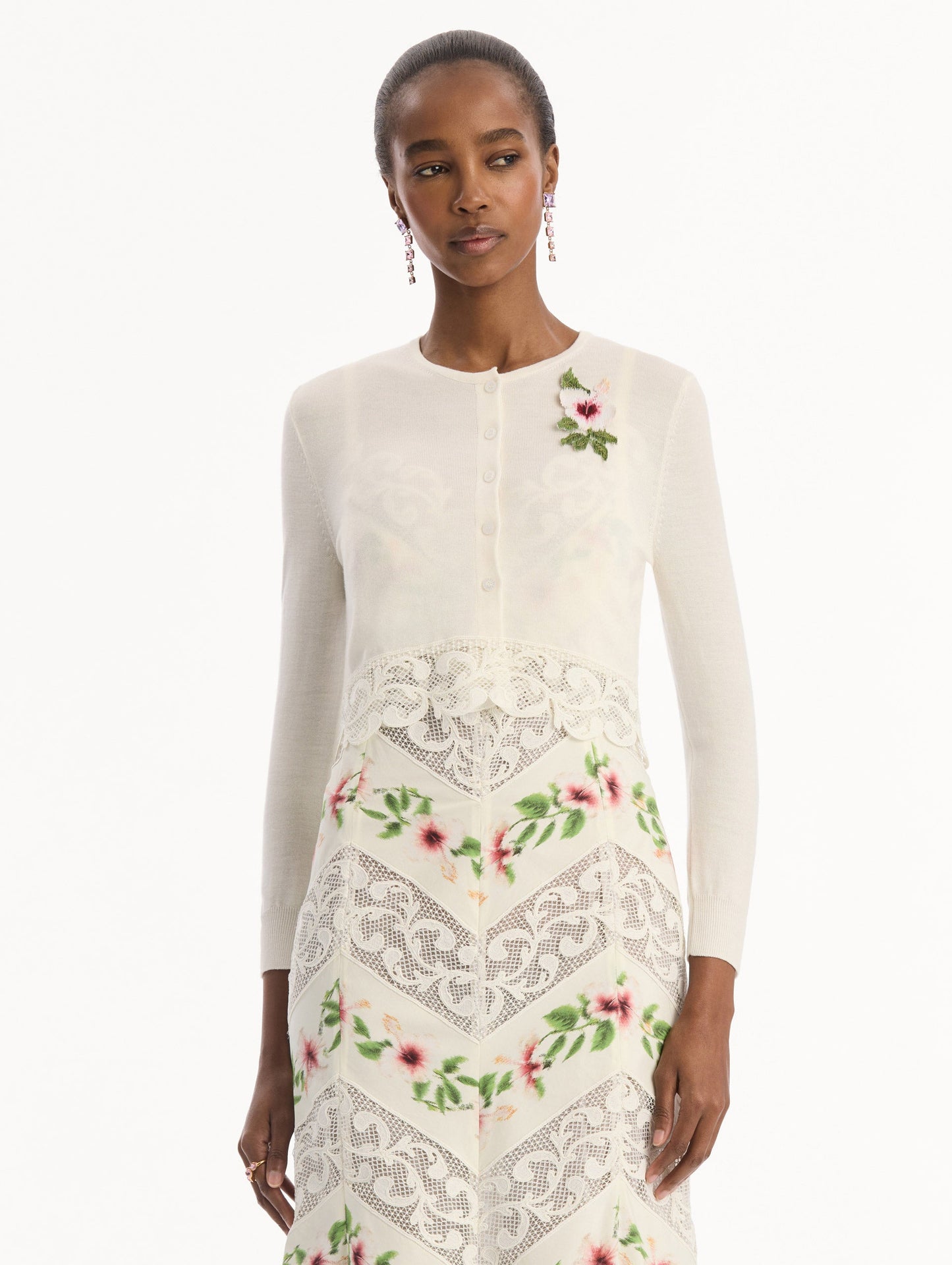 The model is wearing the Chiné Hibiscus Threadwork Cropped Cardigan in Ivory. Featuring a threaded Chiné hibiscus and intricate guipure lace trim. Front View.