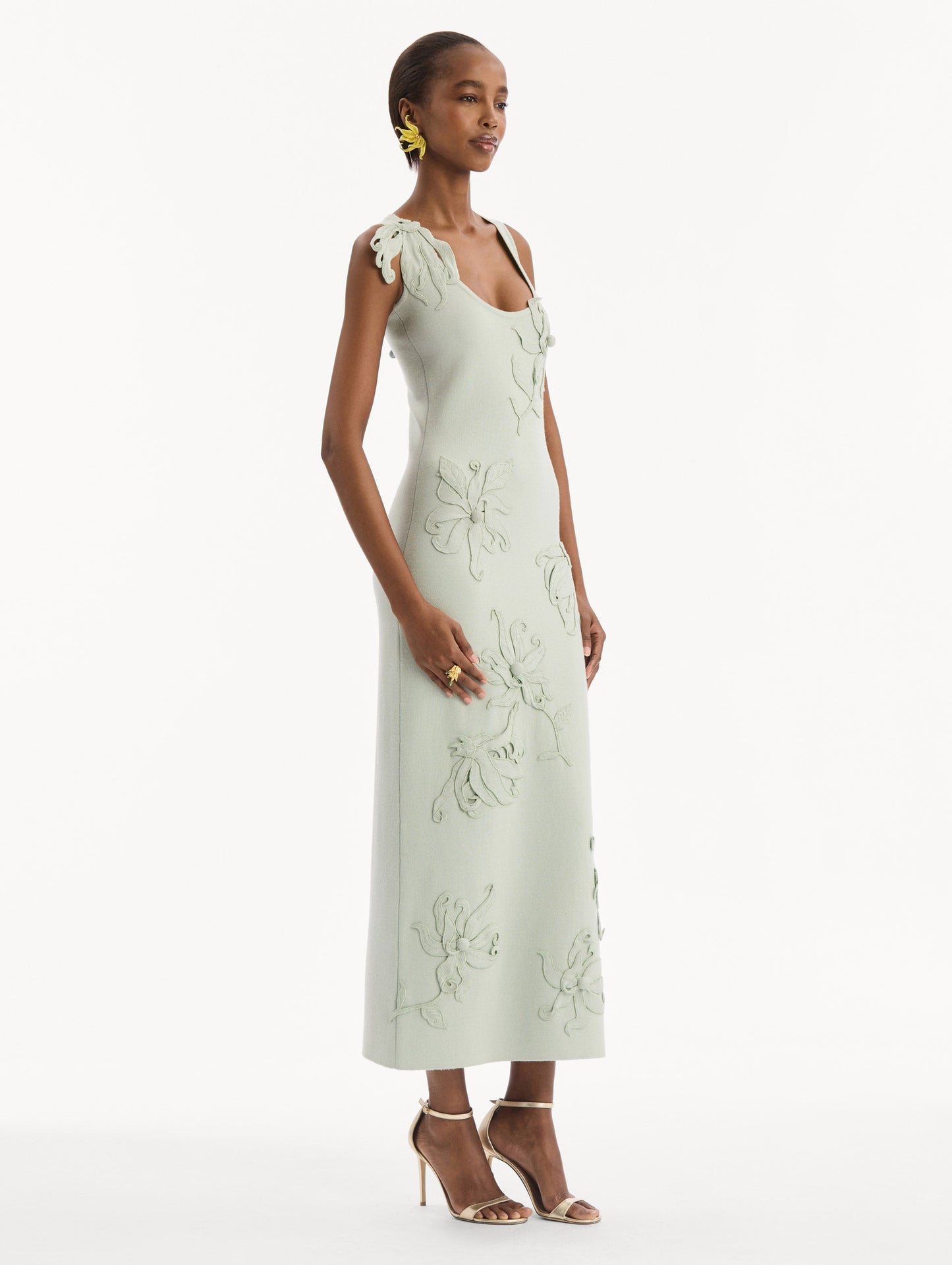 The model is wearing the Hibiscus Embroidered Knit Pencil Dress in Saltwater Blue. Featuring a structural hibiscus embroidery, a scoop neckline, and midi length. Side View.