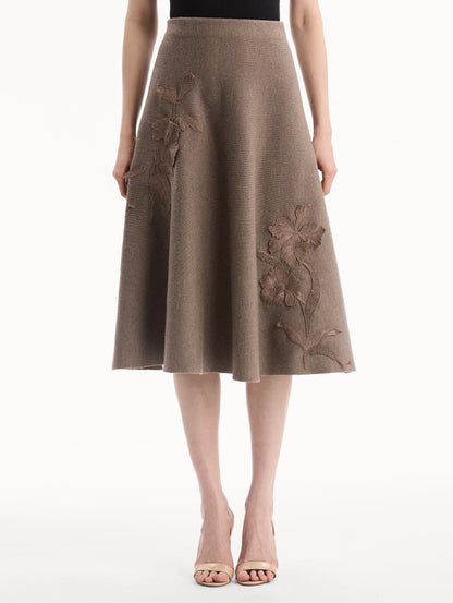 The model is wearing the Hibiscus Embroidered Knit Skirt. Featuring a softly flared silhouette and midi length. Front View.