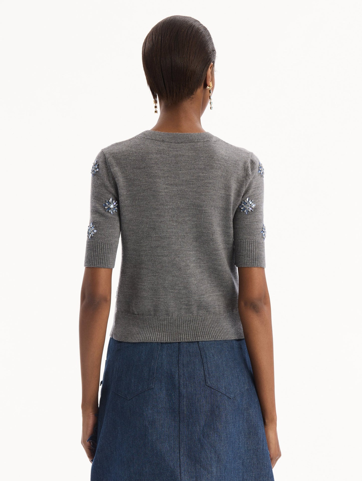 The model is wearing the Crystal Embroidered Pullover in grey with blue crystal embroidered. Featuring a crew neckline and ribbed trims. Back View.