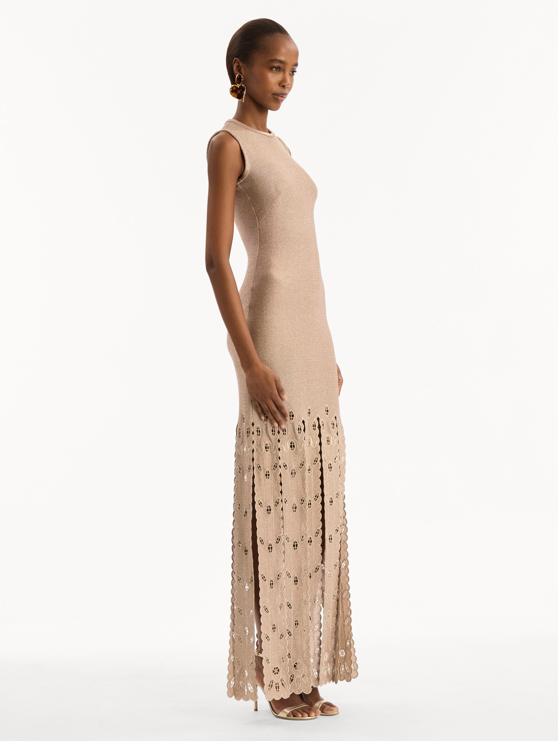The model is wearing the Pineapple Fringe Metallic Jersey Dress. Featuring shimmering metallic jersey fabrication, a body-skimming silhouette, and pineapple-inspired fringe along the hem. Side View.