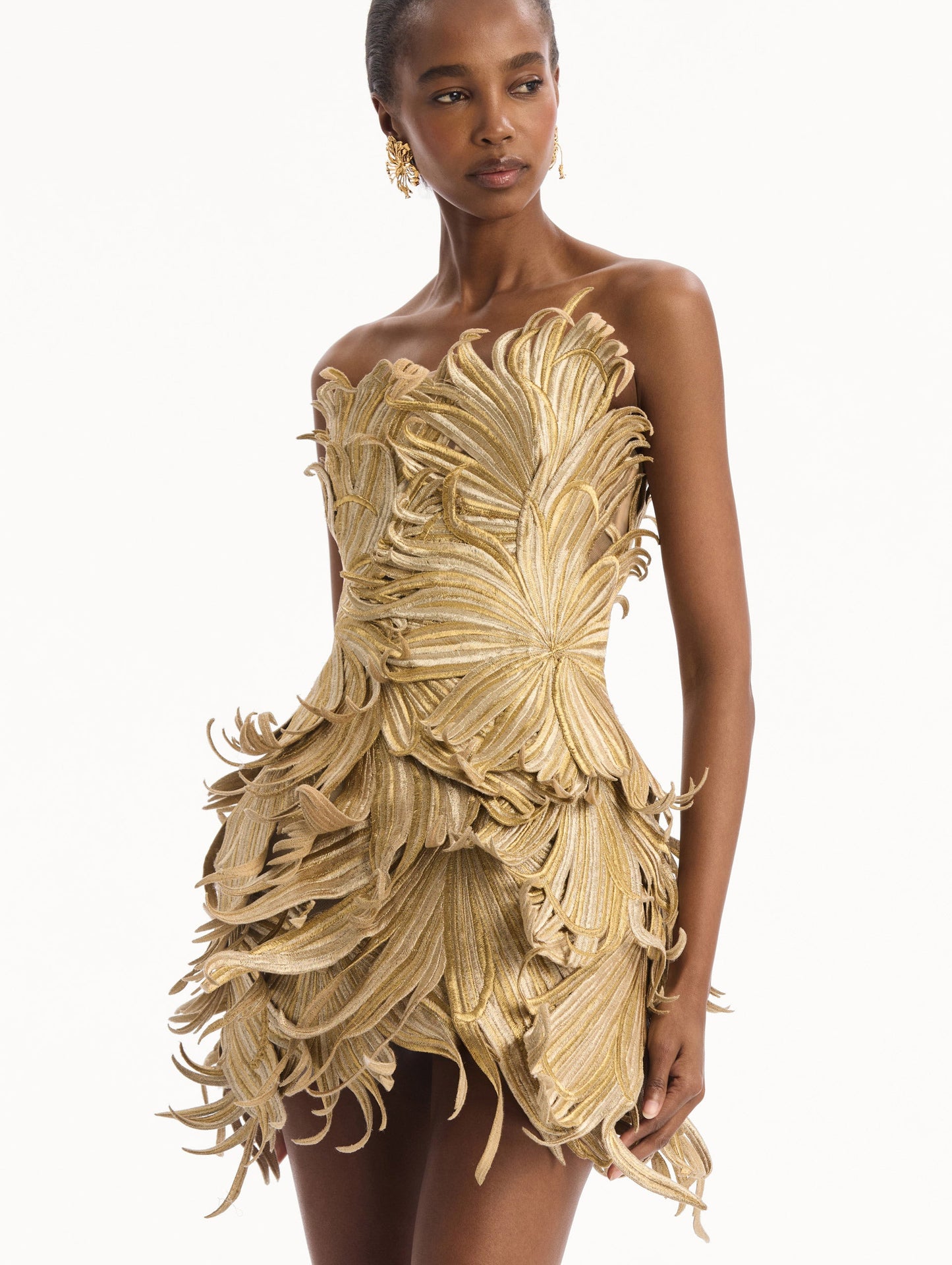 The model is wearing the Palm Leaves Metallic Cocktail Dress in Gold. Featuring dynamic palm leaves sculpted in metallic embroidery and a mini-length skirt. Detail View.