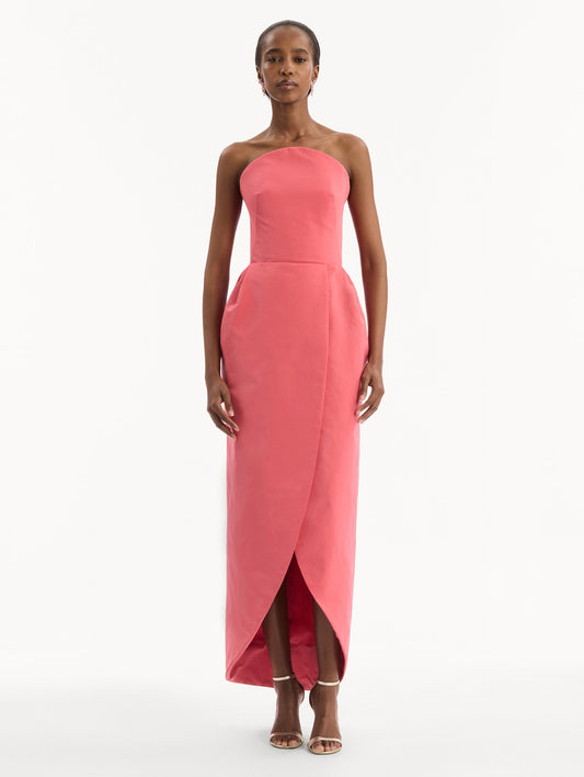 The model is wearing the Strapless Faille Gown in Guava Pink. Featuring a sculpted silhouette and wrap-style skirt with an asymmetrical hem. Front View.