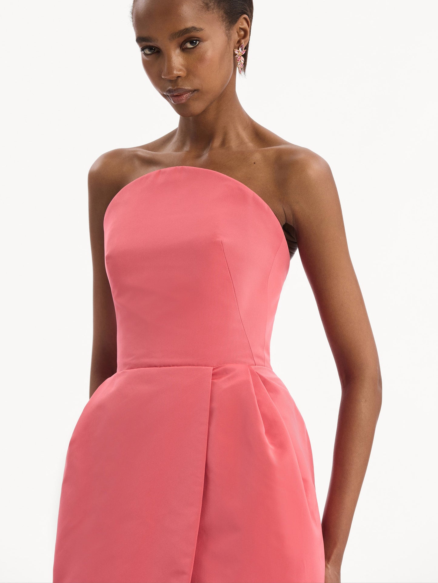The model is wearing the Strapless Faille Gown in Guava Pink. Featuring a sculpted silhouette and wrap-style skirt with an asymmetrical hem. Detail View.