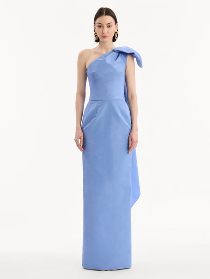 The model is wearing the Bow-Detail Faille Column Gown in a periwinkle blue. Featuring a column silhouette and sculptural bow detail at the shoulder. Front View.