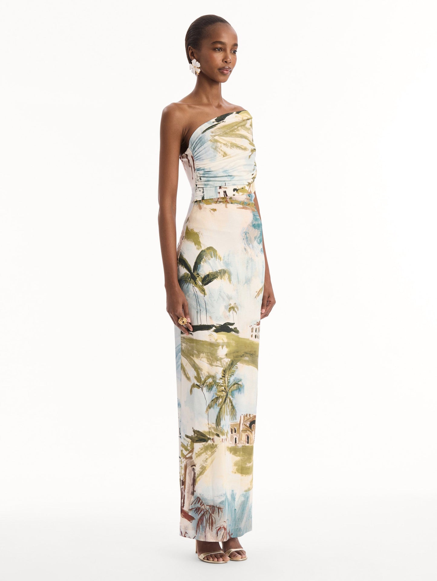 The model is wearing the Dominican Landscape Jersey Gown. Featuring a one-shoulder neckline and long, column silhouette. Side View.