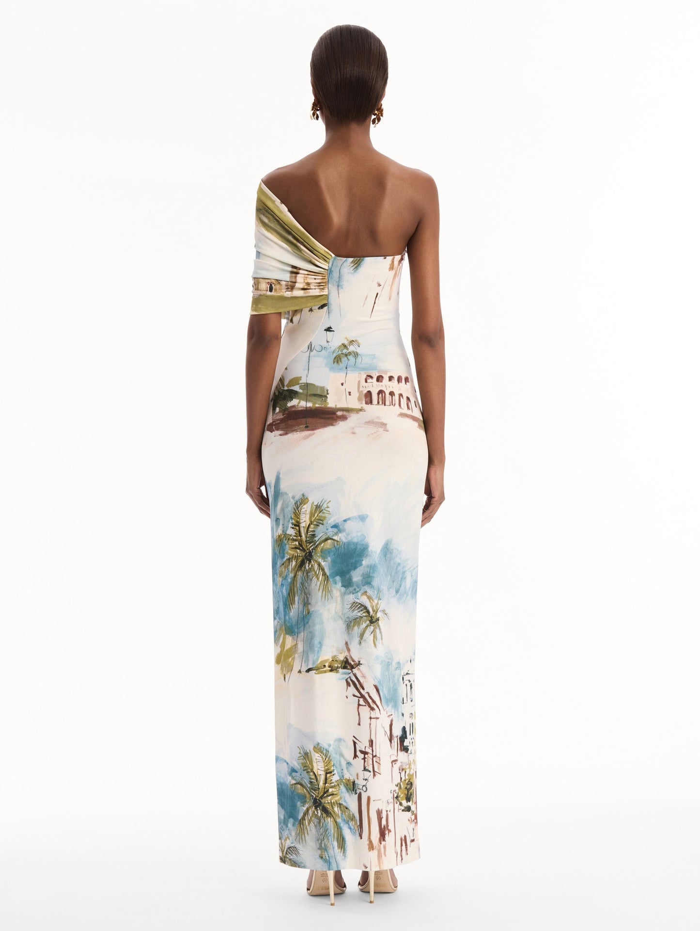 The model is wearing the Dominican Landscape Jersey Gown. Featuring a one-shoulder neckline and long, column silhouette. Back View.