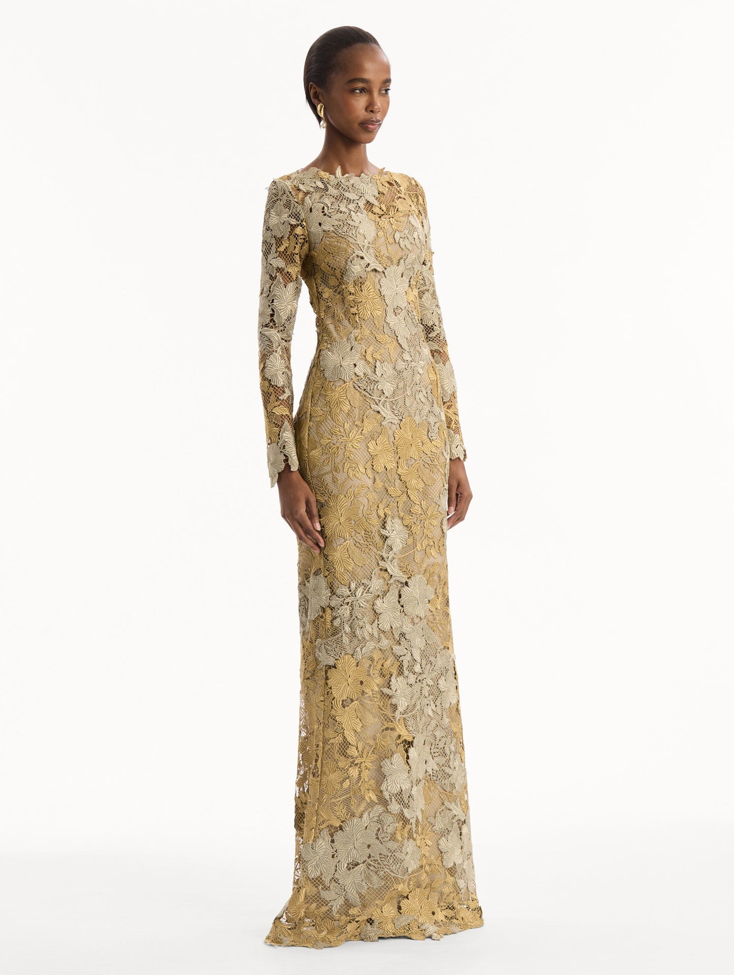 The model is wearing the Hibiscus Metallic Guipure Gown. Featuring metallic guipure lace, long sleeves, a fitted silhouette, and long skirt. Side View.