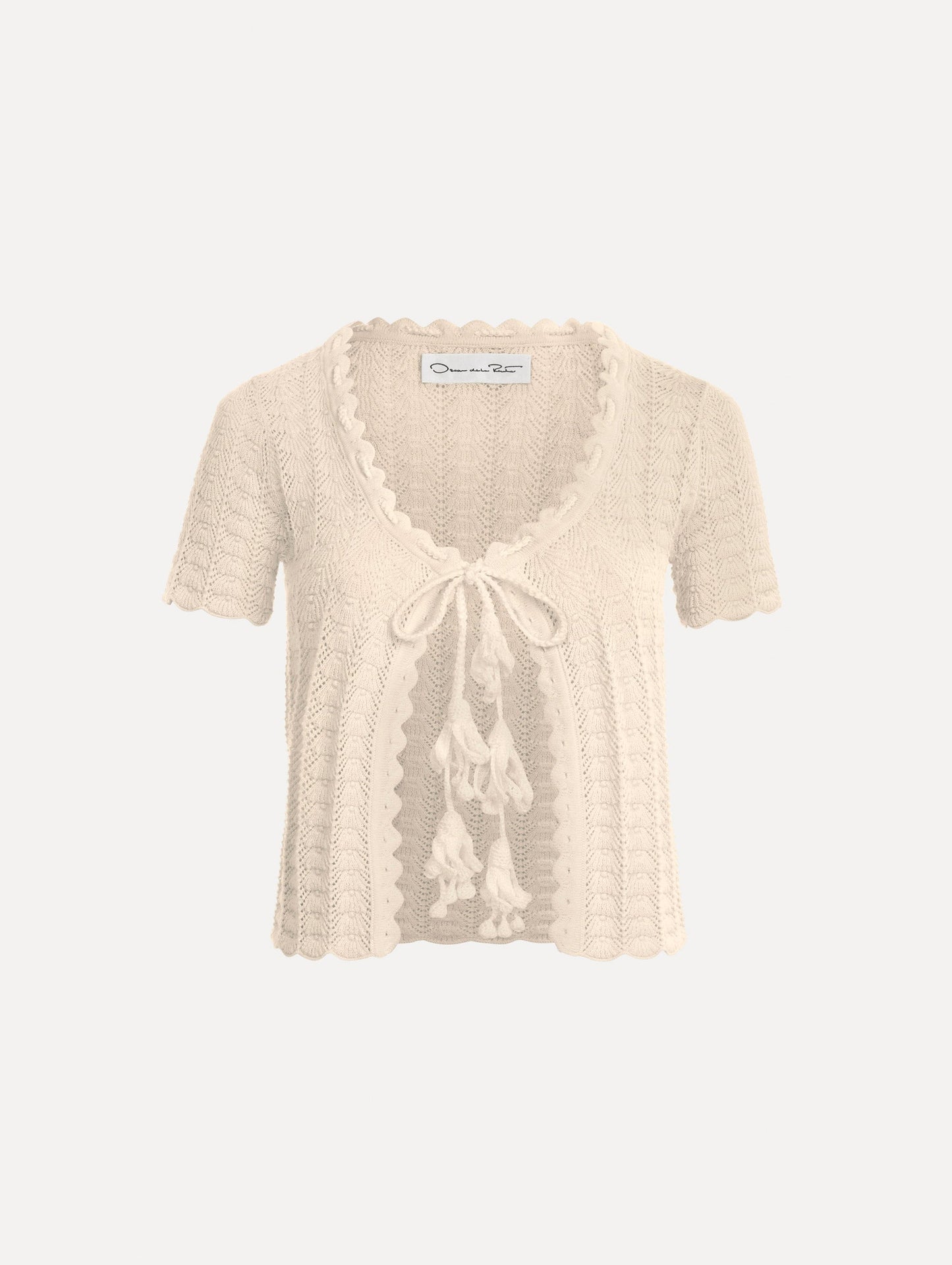 The Pointelle Weave Cardigan in Ivory. Featuring a scoop neckline, short sleeves, scalloped edges, and a front tie closure. Front View.