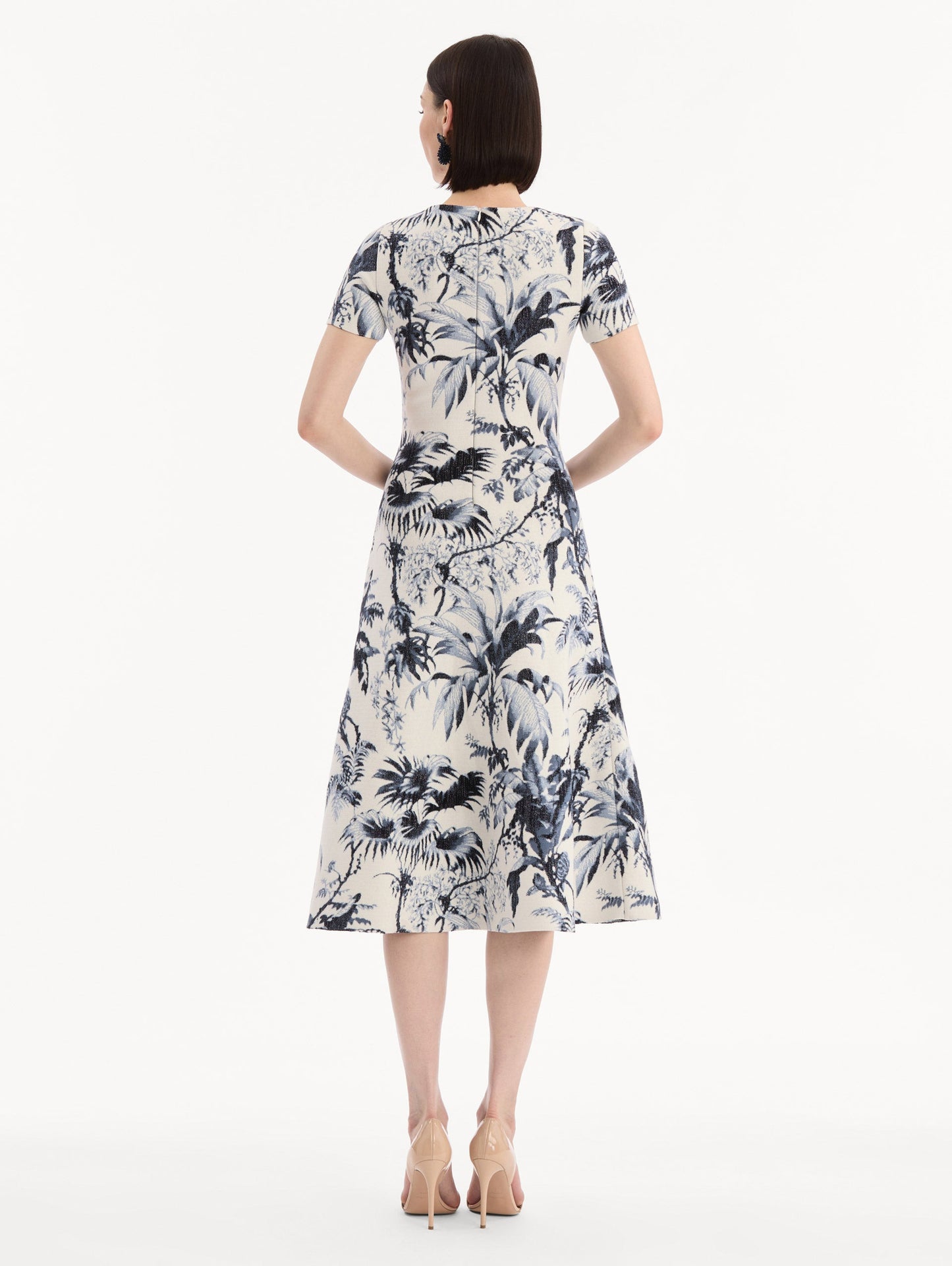 The model is wearing the Chiné Palm Leaves Knit Dress in Navy and Ivory. Featuring a classic silhouette with short sleeves and an A-line midi skirt. Back View.