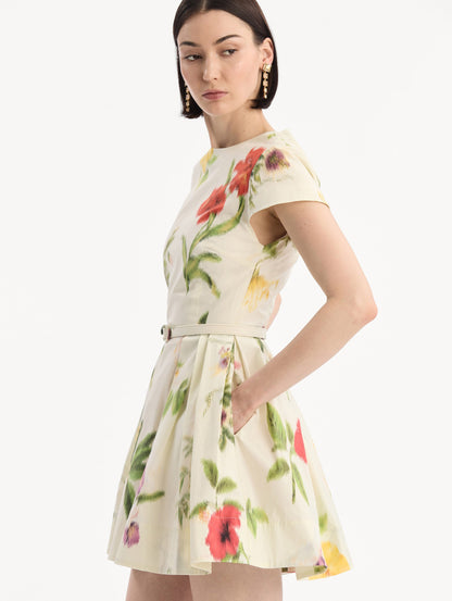 The model is wearing the Chiné Dominican Mixed-Floral Cotton Poplin Dress in Ivory printed with an array of Dominican florals. Featuring cap sleeves, belt at waist, and gathered mini skirt. Detail View.