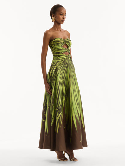 The model is wearing the Palm Leaves Silk Twill Cocktail Dress. Featuring a strapless silhouette, subtle cut-outs at the bodice, and a long skirt. Side View.