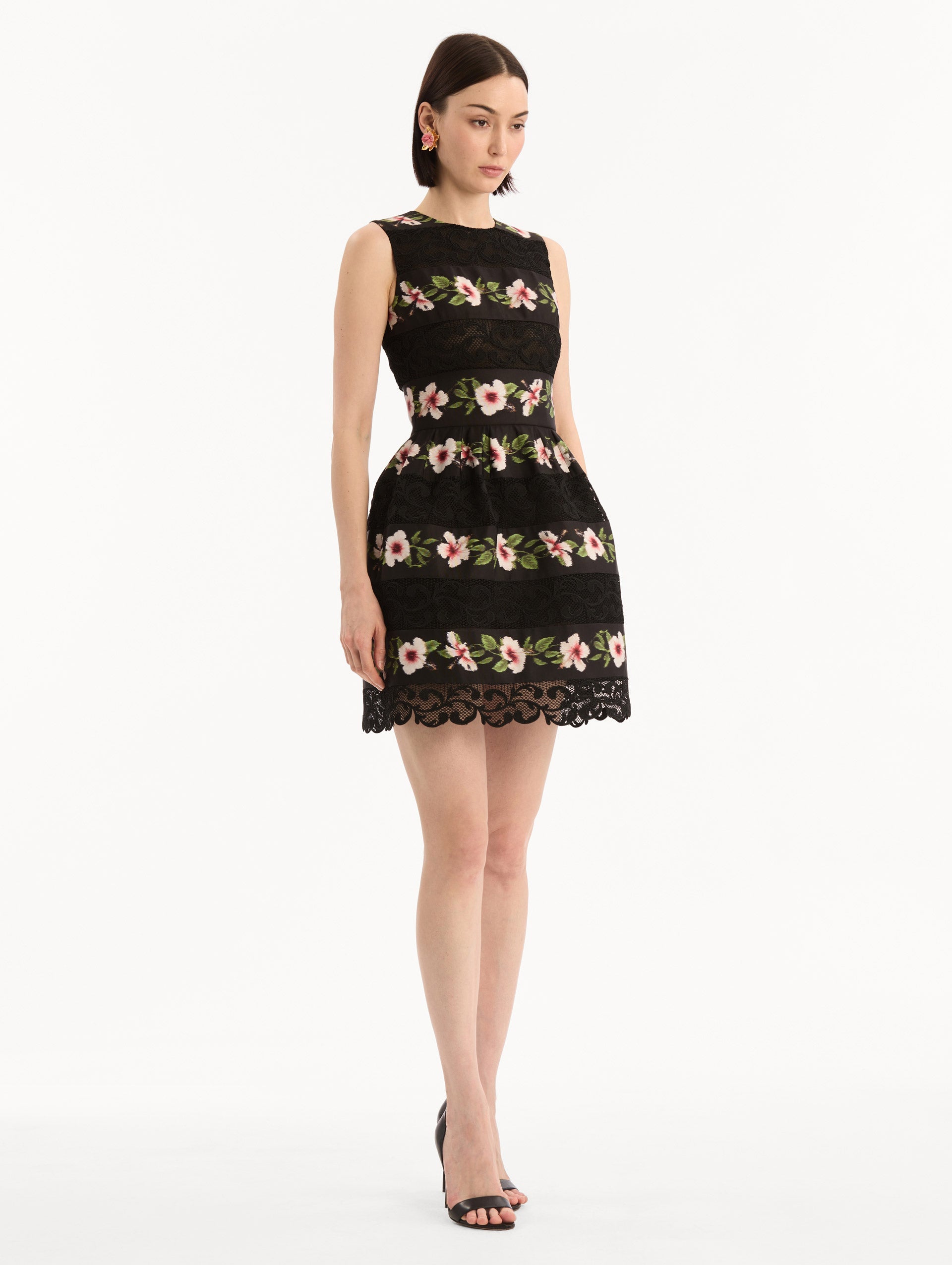 The model is wearing the Chiné Hibiscus Striped Faille Dress in Black. Featuring woven hibiscus motifs alternating with panels of faille and guipure lace, creating a striped pattern. Mini length. Side View.
