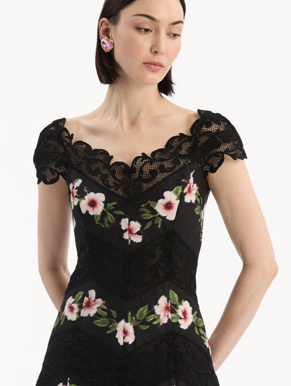 The model is wearing the Chiné Hibiscus Striped Faille Midi Dress in Black. Featuring off-the-shoulder cap sleeves, a midi length, and woven hibiscus motifs alternating with panels of faille and guipure lace, creating a striped composition. Detail View.