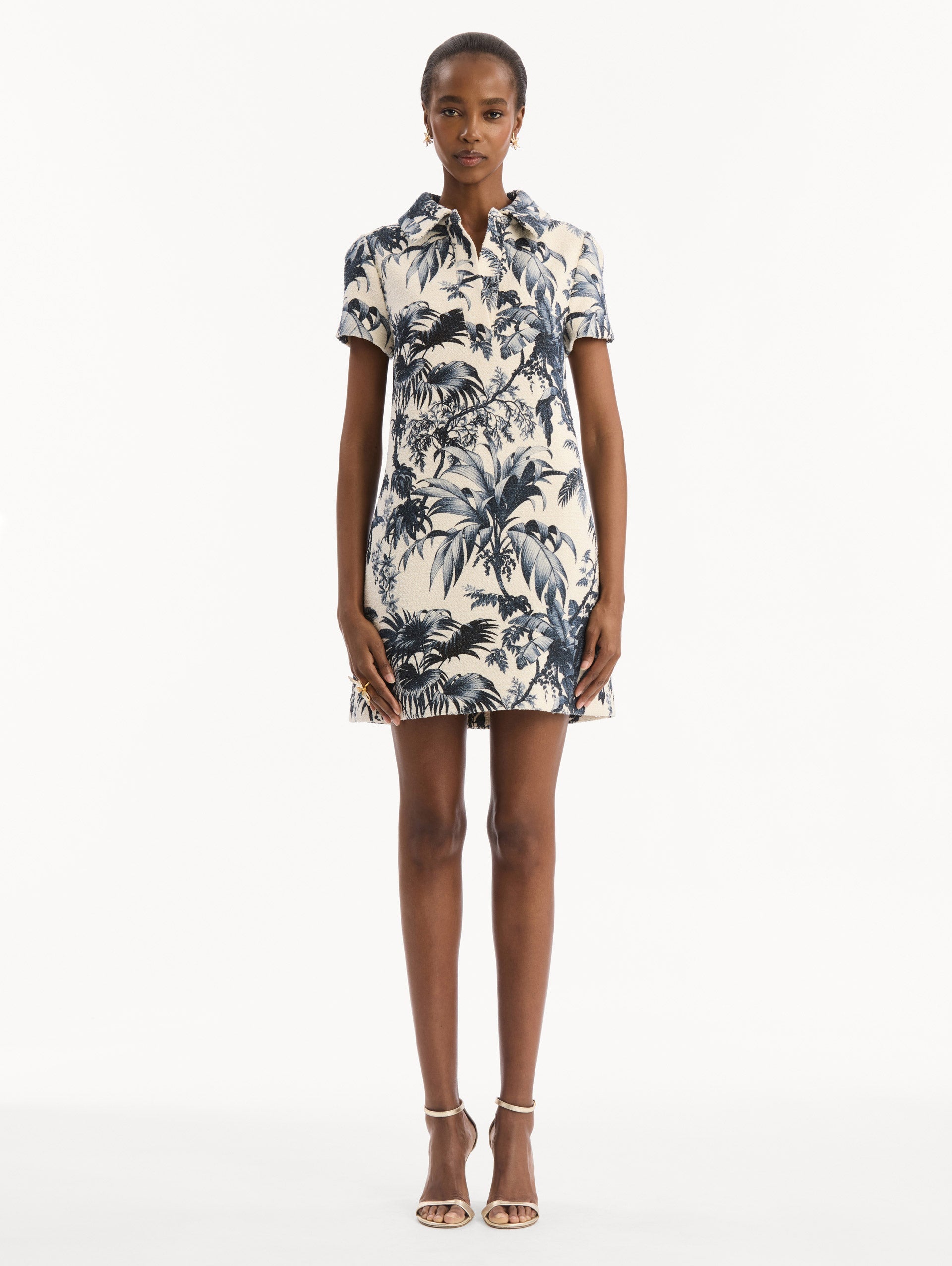 The model is wearing the Chiné Palm Leaves Shift Dress in ivory printed with navy palm leaves. Featuring a classic collar neckline, short sleeves, and mini length. Front View.