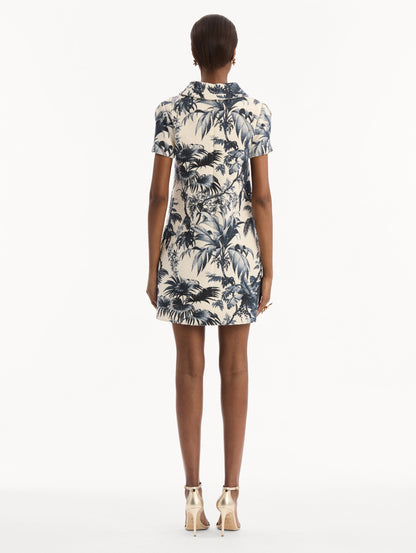 The model is wearing the Chiné Palm Leaves Shift Dress in ivory printed with navy palm leaves. Featuring a classic collar neckline, short sleeves, and mini length. Back View.