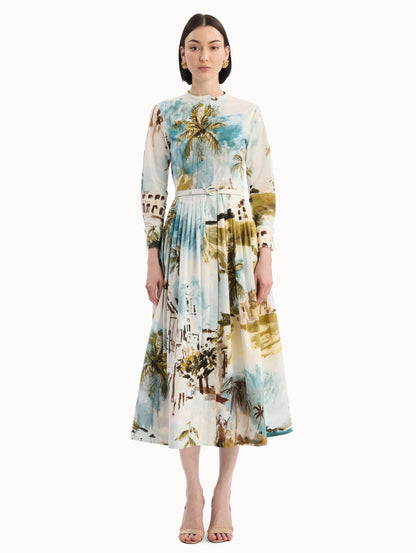 The model is wearing the Dominican Landscape Cotton Poplin Short-Sleeve Dress printed with the Dominican landscape. Featuring long sleeves, front-button closure, belt at waist, and pleated midi skirt. Front view.