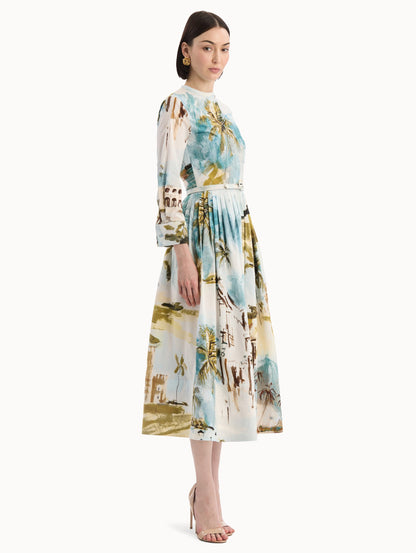The model is wearing the Dominican Landscape Cotton Poplin Short-Sleeve Dress printed with the Dominican landscape. Featuring long sleeves, front-button closure, belt at waist, and pleated midi skirt. Side View.