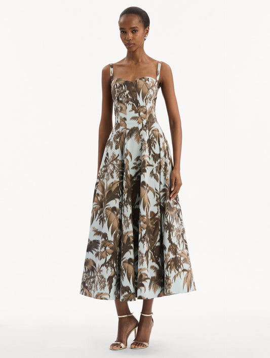 The model is wearing the Chiné Palm Leaves Cotton Poplin Dress in light blue printed with brown palm leaves. Featuring a subtle sweetheart neckline with tank straps, a softly structured bodice, and flowing midi skirt. Front View.