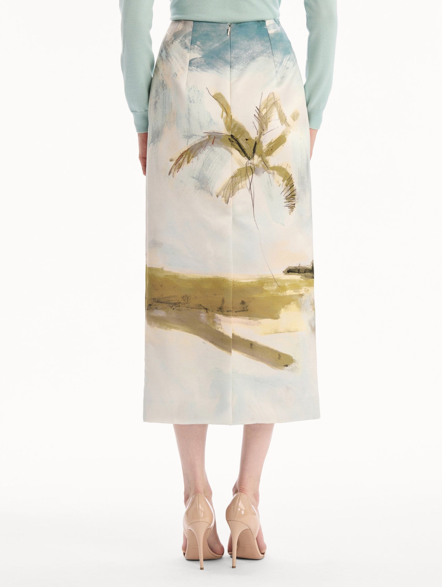 The model is wearing the Dominican Landscape Pencil Skirt printed in the Dominican landscape. Featuring a structured, column silhouette and midi length. Back View.