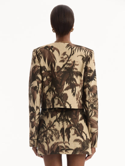 The model is wearing the Chiné Palm Leaves Jacket printed with brown palm leaves. Featuring long sleeves, front pockets with a button closure, and a tailored silhouette. Back View.