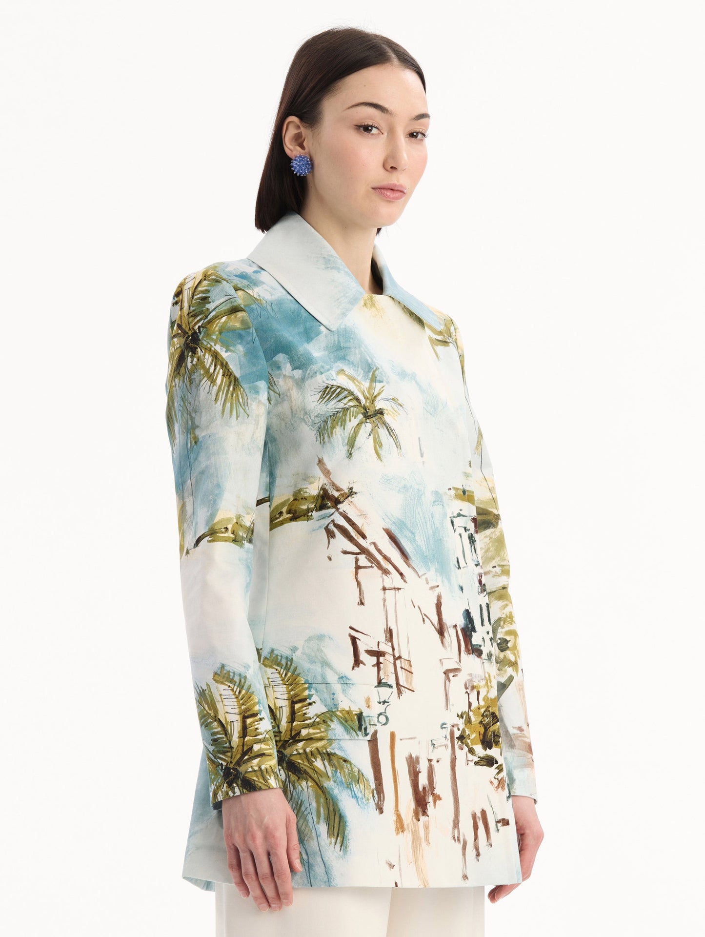 The model is wearing the Dominican Landscape Cotton Poplin Coat featuring an exaggerated collar, hidden buttons, front-flap pockets, and long sleeves. Side View.